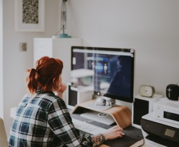 Une femme rousse est assise devant son écran d'ordinateur